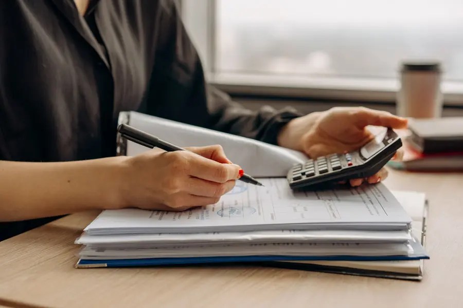 Finance manager working through capital allowance figures with a calculator and a ring binder of accounts
