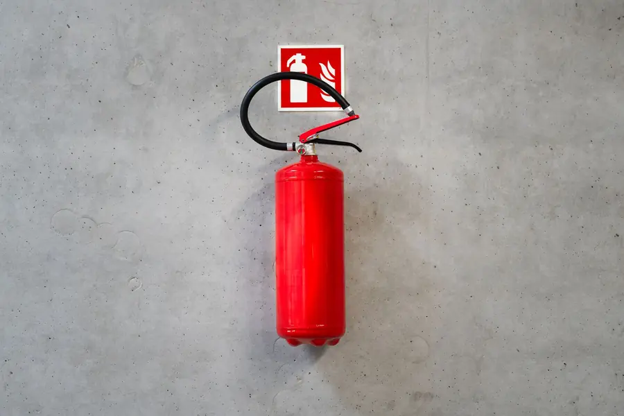 Red fire extinguisher and safety sign mounted on a concrete wall, part of planning fire safety for a commercial battery