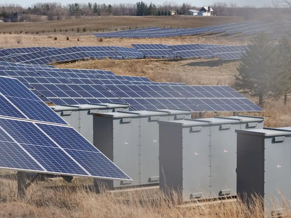 Grey outdoor battery storage cabinets lined up in front of ground-mounted solar panels