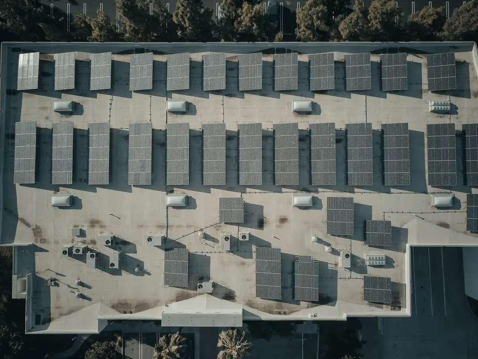 Aerial view of a commercial flat roof with rows of solar PV panels set around rooftop plant and roof lights